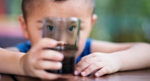 Cute boy looking at camera through a water glass in restaurant.