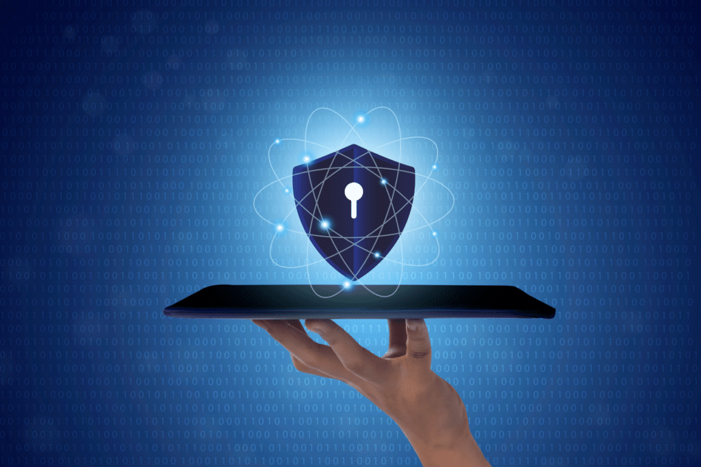 A stock image of a closed laptop resting on a man's fingertips, with a illustration of a security shield hovering above it.