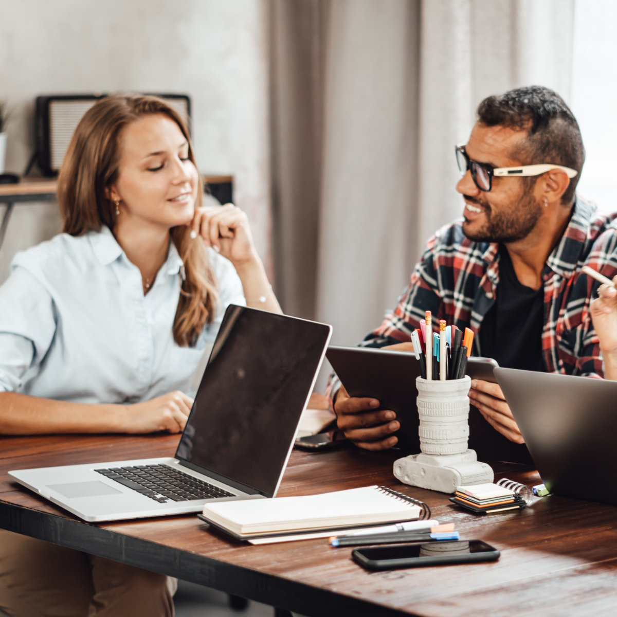 Man and woman sitting at a table with a pencil cup, notepads, and their laptops discussing technical needs.
